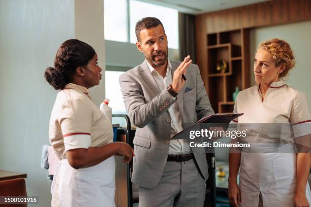 shift manager explaining procedure to two diverse housekeepers - cleaner man uniform stock pictures, royalty-free photos & images