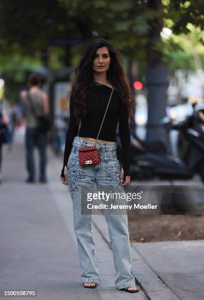 Fashion Week guest is seen wearing gold chains, asymmetric black cropped top, Valentino Rockstud red leather crossbody mini bag, sparkling wide leg...