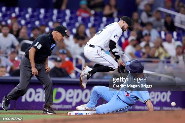 Matt Chapman of the Toronto Blue Jays slides safely to third base under Jon Berti of the Miami Marlins during the fifth inning at loanDepot park on...
