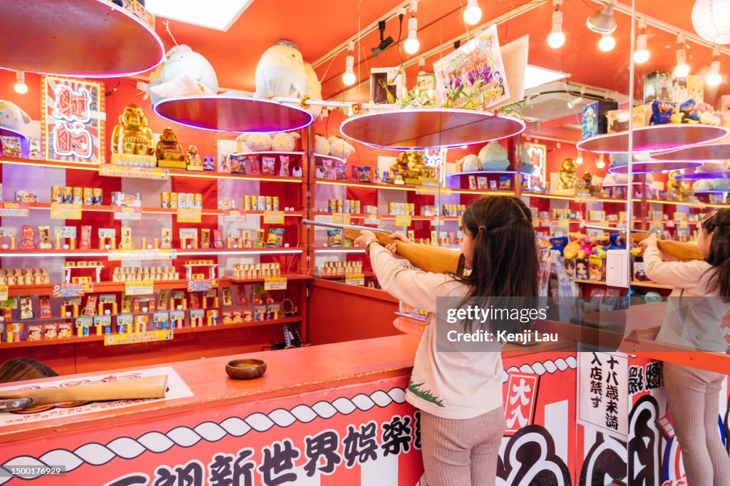 Little Asian girl playing traditional shooting game to win prizes in Osaka, Japan when she visits Japan with her family. Concept of travelling, leisure and vacation.