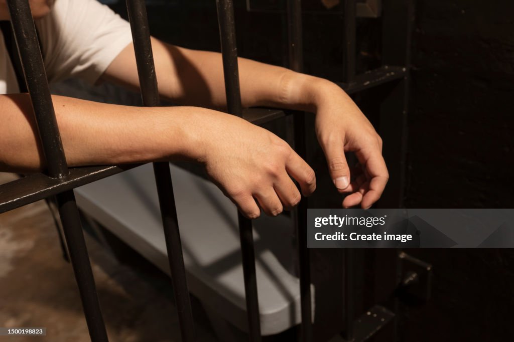 Hands of Prisoner behind bars in Prison Cell.
