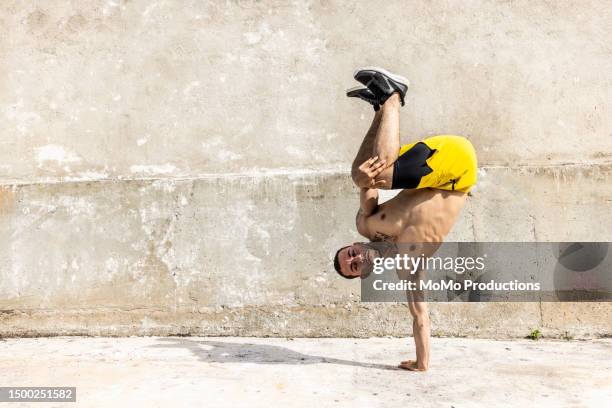 male athlete holding breakdancing pose in front of concrete wall - koordination stock-fotos und bilder