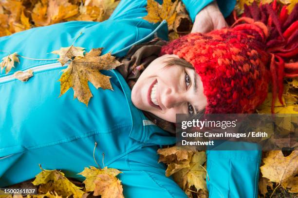 close-up of smiling woman lying on ground in heap of autumn leaves - edith falls stock pictures, royalty-free photos & images