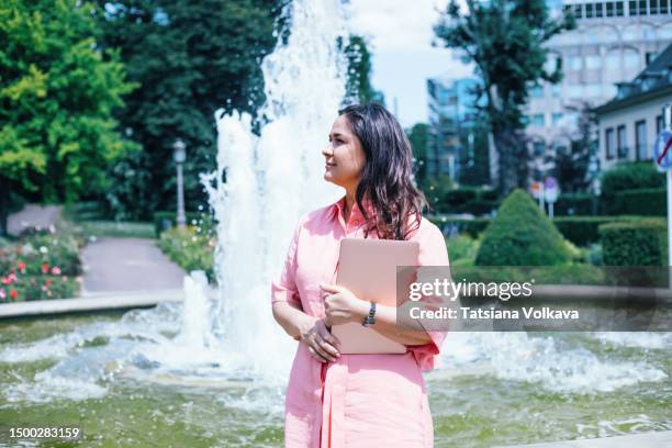 charming business woman in pink shirt dress standing by fountain waiting for potential client - luxembourg stock pictures, royalty-free photos & images