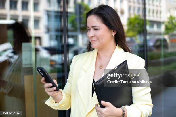 mature woman in trendy yellow blazer standing on street looking at phone screen smiling - iphone case stock pictures, royalty-free photos & images