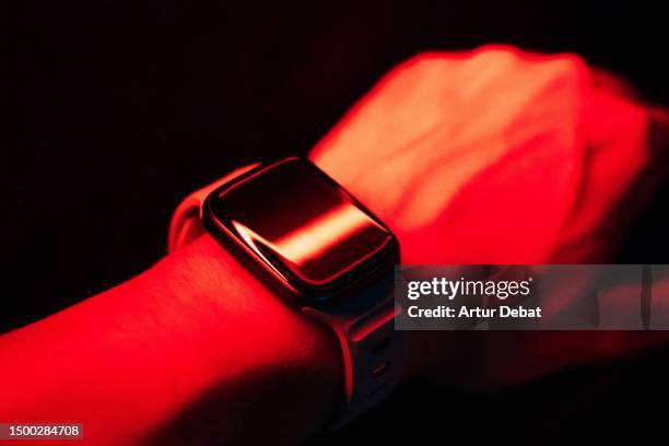 smart watch on wrist illuminated with red light in dark scenario. - android apps stock pictures, royalty-free photos & images