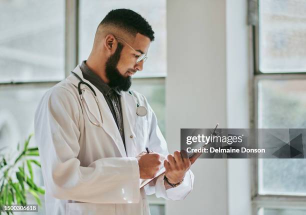side view of a  young male doctor stands while looking down at a document and reading, with copy space. stock photo - clipboard and glasses imagens e fotografias de stock
