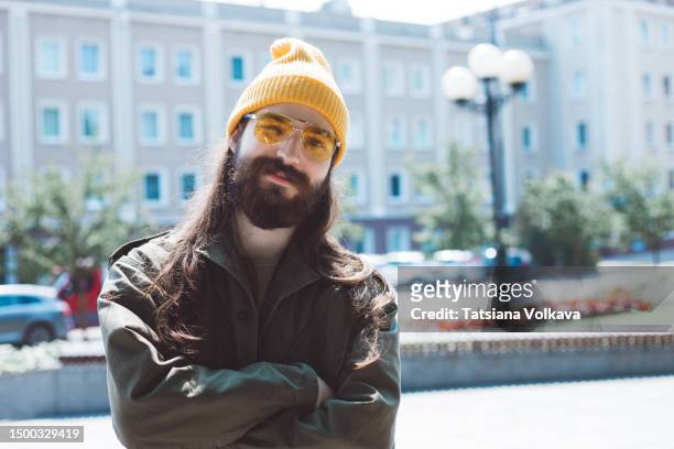 easygoing college student with brown hair and beard in yellow beanie and yellow glasses standing on street - brown hat 個照片及圖片檔