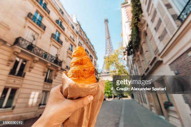 man holding croissant next to eiffel tower, personal perspective view, paris, france - croissant stockfoto's en -beelden