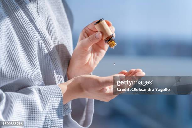 woman in bathrobe dripping essential oil on hand. aroma oil in a small glass amber bottle with craft label. - tea tree oil stock pictures, royalty-free photos & images
