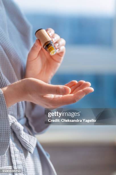woman in bathrobe dripping essential oil on hand. aroma oil in a small glass amber bottle with craft label. - peppermint geranium stock pictures, royalty-free photos & images