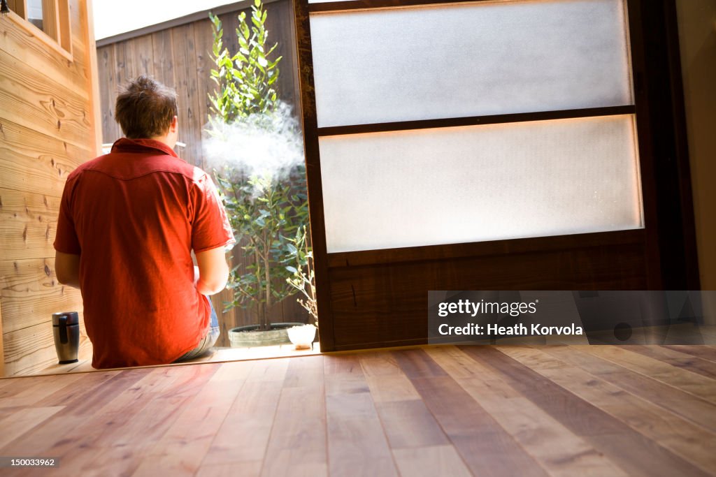 Man sits out of Japanese house to smoke.