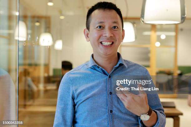 front view of an asian businessman working in a modern office space, engaging in a video conference with his business partners on a computer while speaking in front of the webcam - in front of camera stock pictures, royalty-free photos & images