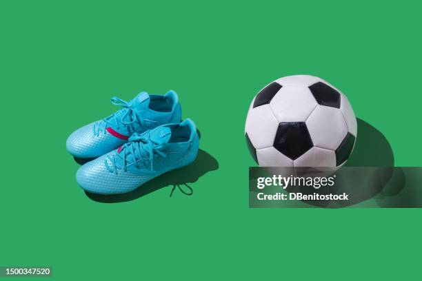 blue soccer boots next to black and white retro ball, on green background. soccer, sports shoes and women's soccer concept. - stollenschuh stock-fotos und bilder