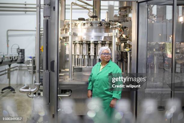 female operator at automatic liquid filling machine in water bottling plant - bottling plant stock pictures, royalty-free photos & images