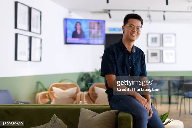 a portrait depicts a young and energetic asian college student sitting on a couch in the school campus, radiating positivity with a bright smile on his face. - insight tv stock pictures, royalty-free photos & images