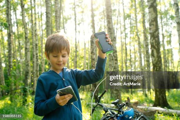 der kleine junge verwendet eine tragbare solarbatterie, um das smartphone in der natur aufzuladen. nachhaltiger lebensstil, ökologische alternative energien und ökologische konzepte. - powerbank stock-fotos und bilder