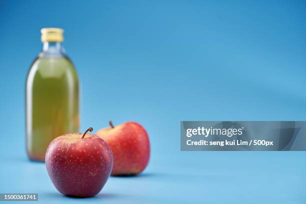 close-up of apple and bottle on table against blue background - apple cider vinegar stock pictures, royalty-free photos & images