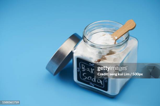 close-up of baking soda in jar on table against blue background - baking powder stock pictures, royalty-free photos & images