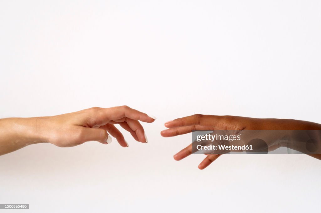 Cropped image of friends reaching to each other against white background