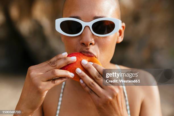 woman wearing sunglasses eating mango at beach - woman eating fruit stock pictures, royalty-free photos & images