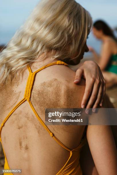 blond woman with sand on back at beach - beach hair stock-fotos und bilder