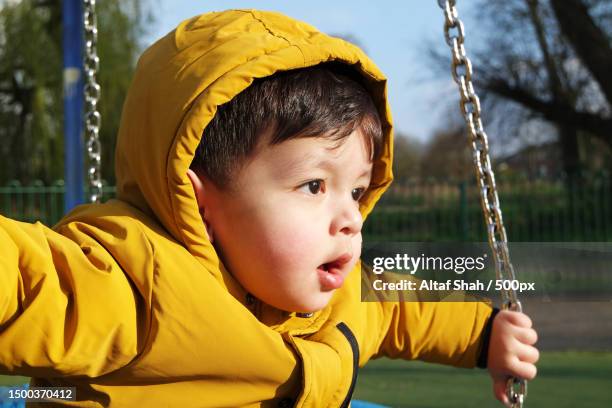 boy looking away while sitting on swing at playground,luton,united kingdom,uk - peel park stock pictures, royalty-free photos & images