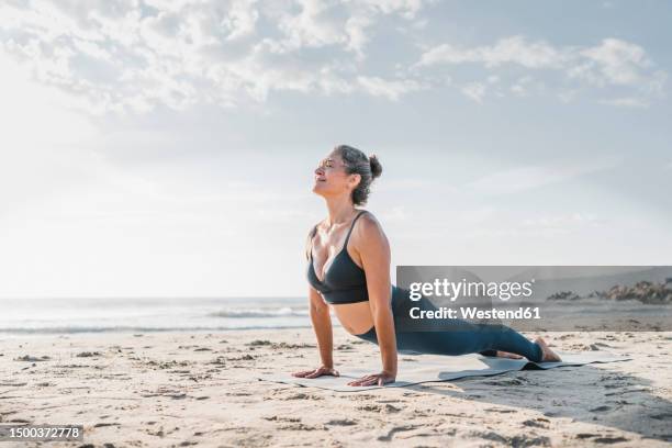 woman practicing yoga with cobra pose in front of sky at beach - cobra stretch stock pictures, royalty-free photos & images