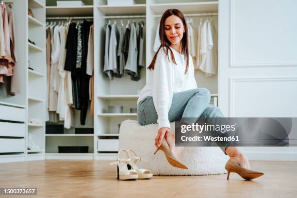 smiling woman trying heels sitting on seat in closet - putting on high heels stock pictures, royalty-free photos & images