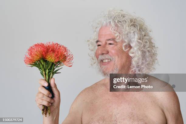 mittlere aufnahme eines kaukasischen alten mannes mit weißen und langen haaren, der lächelt und einen strauß orangefarbener blumen in einem studio hält. - natural portrait studio shot white background stock-fotos und bilder