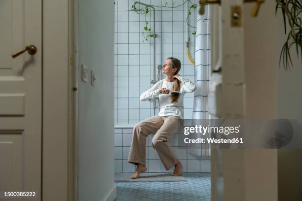 mature woman brushing hair in bathroom at home - brushing hair stock pictures, royalty-free photos & images