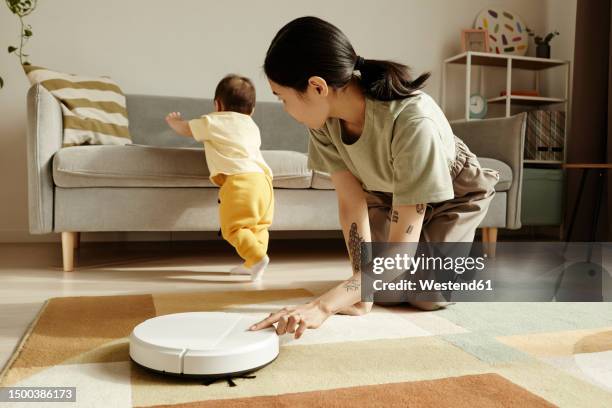 mother turning on robotic vacuum cleaner looking at daughter at home - armenia girls stockfoto's en -beelden