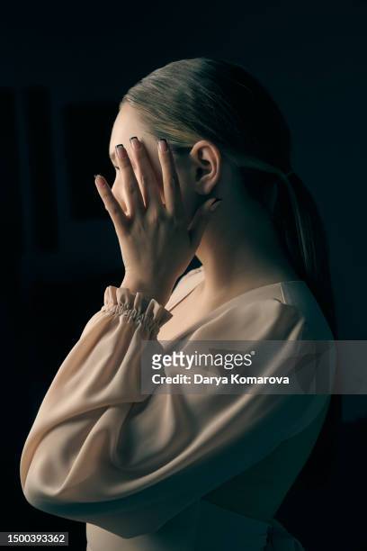 a young woman in a beige dress on a black background stands and covers her face with her hand. the concept of complexes, shyness, manicure, headache, privacy. - camouflage fabric stock pictures, royalty-free photos & images