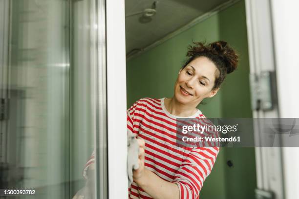smiling woman cleaning window frame - agent de ménage photos et images de collection