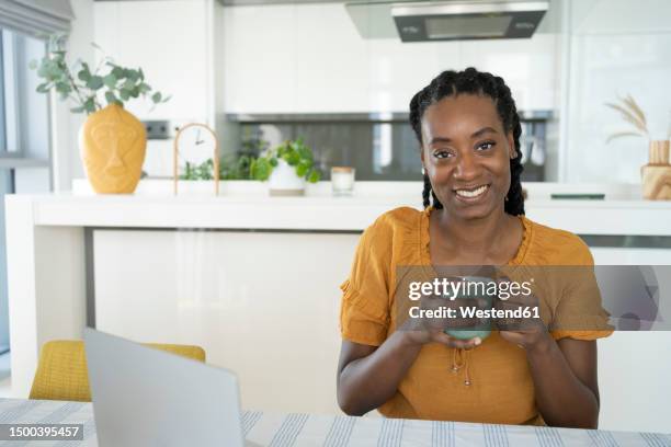 smiling freelancer holding coffee mug at home - portrait frau arabisch frontal stock-fotos und bilder