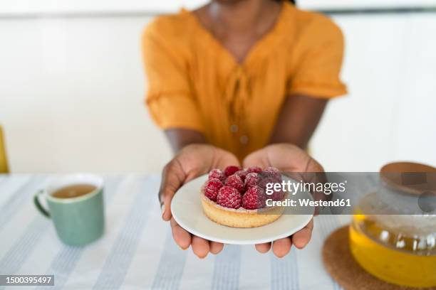 hands of woman holding raspberry tart on plate at home - himbeertörtchen stock-fotos und bilder