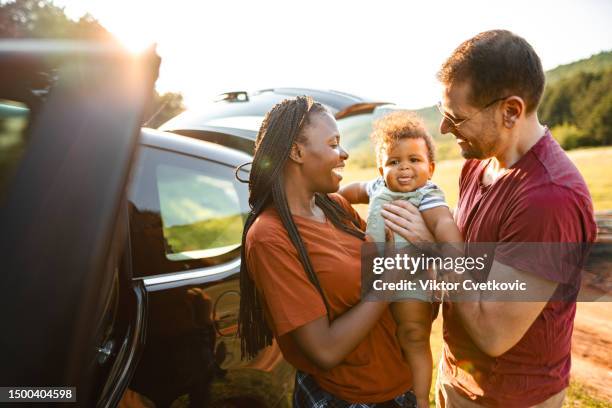 abenteuerlustiges ehepaar mit kleinem baby, das an einem sonnigen tag neben ihrem auto in der natur steht - person gemischter abstammung stock-fotos und bilder