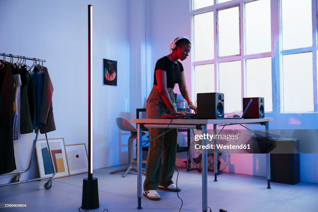 Young DJ wearing headphones and using laptop at home