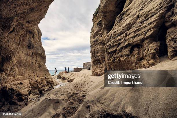 teenage kids jumping over a small stream on a beach. - cliff side stock pictures, royalty-free photos & images