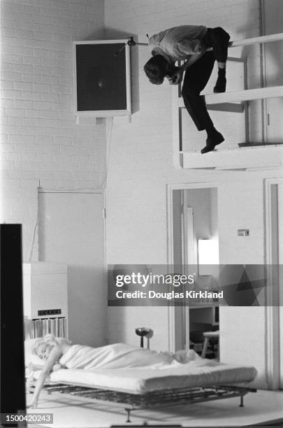 American actress Marilyn Monroe poses on a bed as Canadian-born American photographer Douglas Kirkland perches on an indoor balcony above her during...