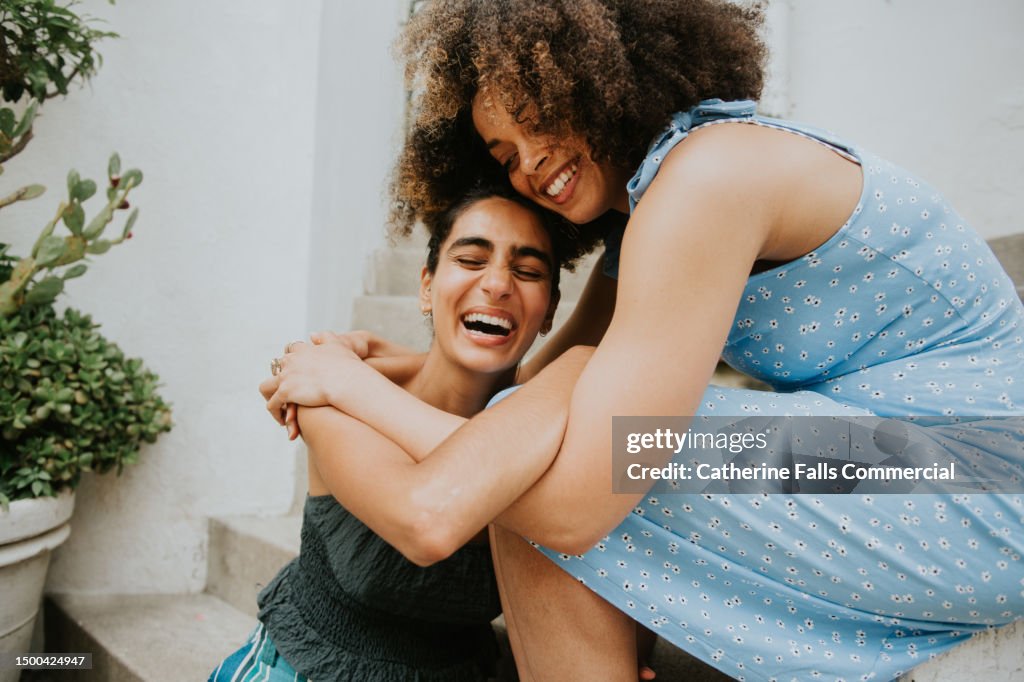 Two beautiful young woman laugh as they affectionately hug