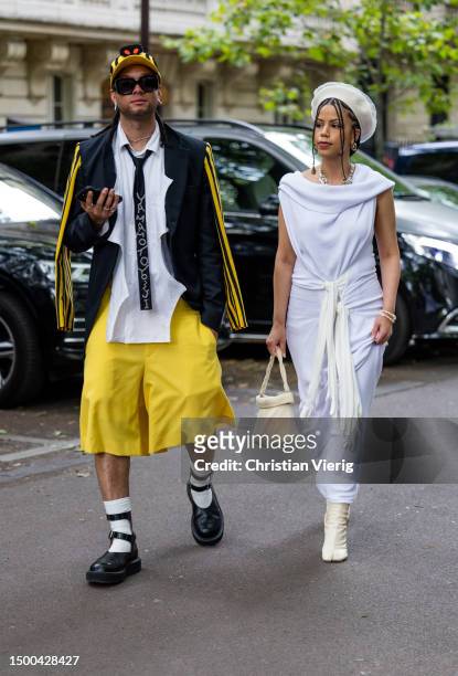 Guest wears yellow shorts, white shirt, jacket & a guest wears wrapped dress, hat outside Rhude during the Menswear Spring/Summer 2024 as part of...