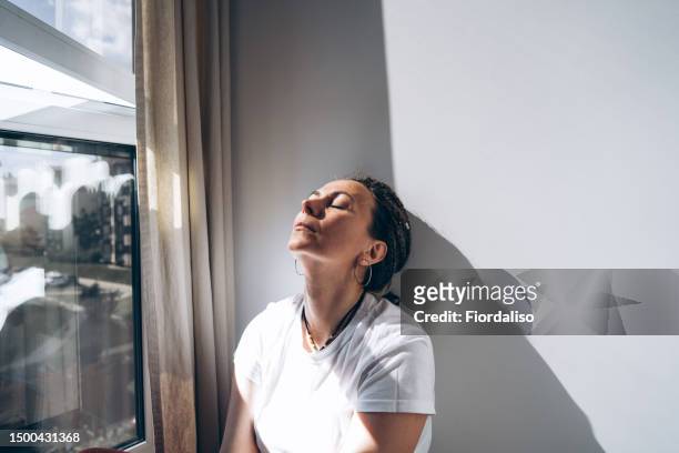 portrait of a woman sitting by the window - donna triste foto e immagini stock
