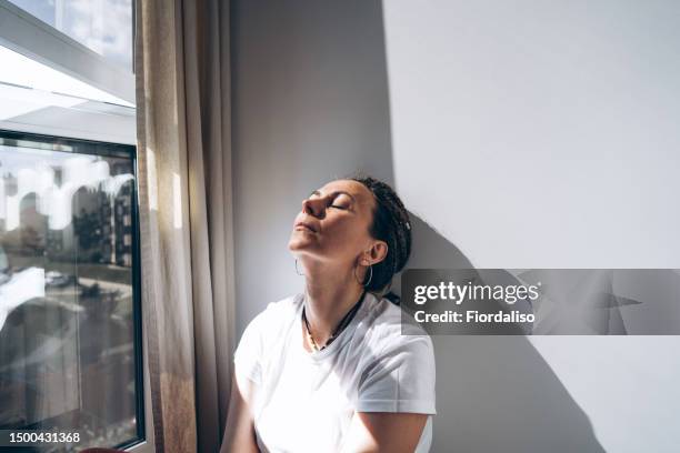 portrait of a woman sitting by the window - sadness concept stock pictures, royalty-free photos & images