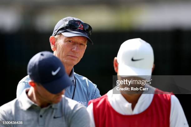 Brad Faxon looks on as Rory McIlroy of Northern Ireland and caddy Harry Diamond talk on the 12th tee during a practice round prior to the Travelers...