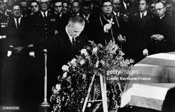 New President of the United States Lyndon Johnson praying on the coffin of President Kennedy at the Capitol behind the wreath of presidency on...