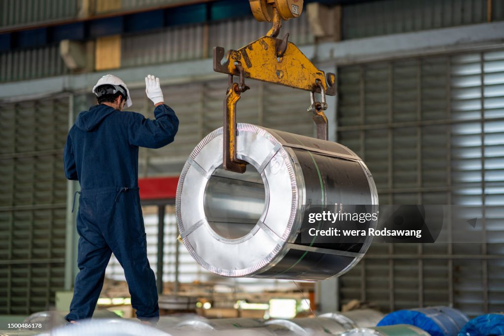 Sheet metal worker controlling lift roll metal sheet crane in storage room