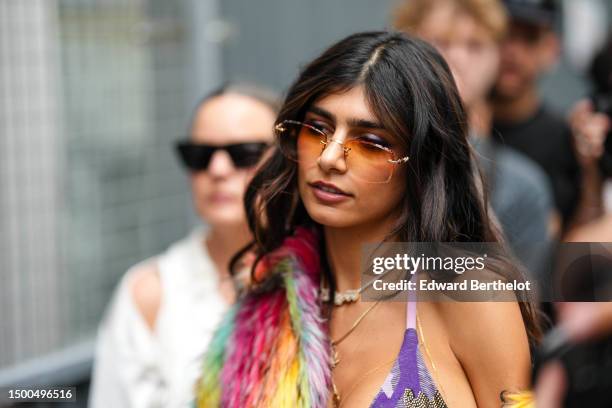 Mia Khalifa wears orange squared sunglasses, gold necklaces, a multicolored print pattern fluffy coat, a dark and pale purple print pattern with...