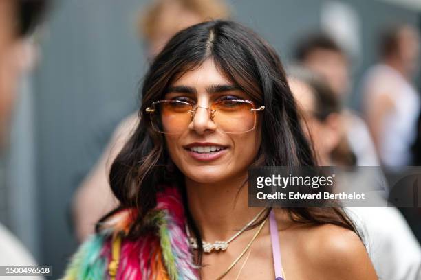 Mia Khalifa wears orange squared sunglasses, gold necklaces, a multicolored print pattern fluffy coat, a dark and pale purple print pattern with...