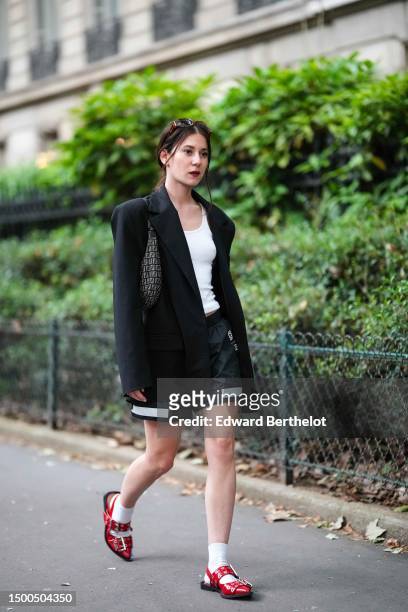 Guest wears a white tank-top, a black oversized blazer jacket, black nylon with large white straps pattern shorts from GCDS, a black and gray FF...